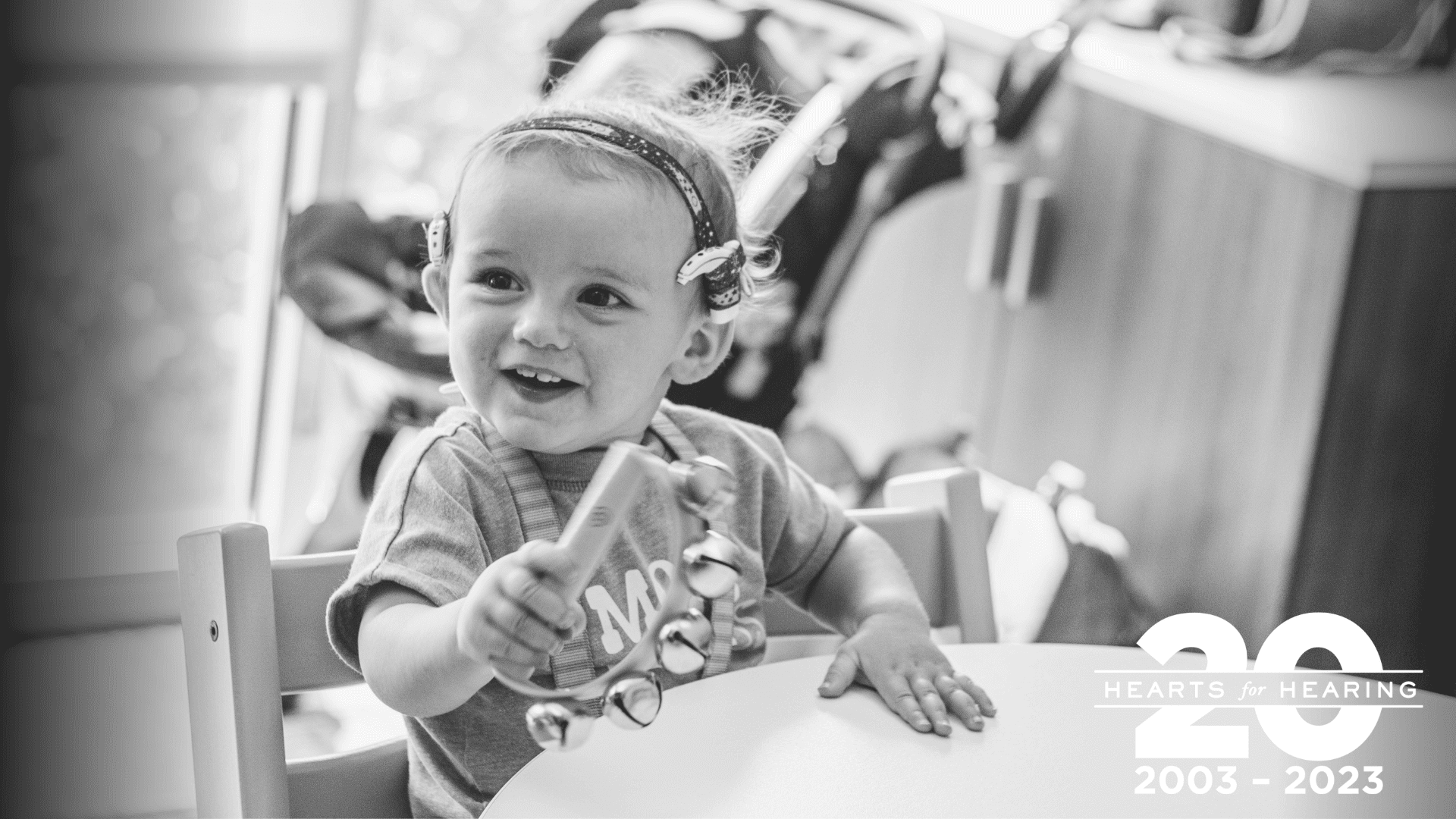 black and white photo of a young boy with cochlear implants shaking a tambourine