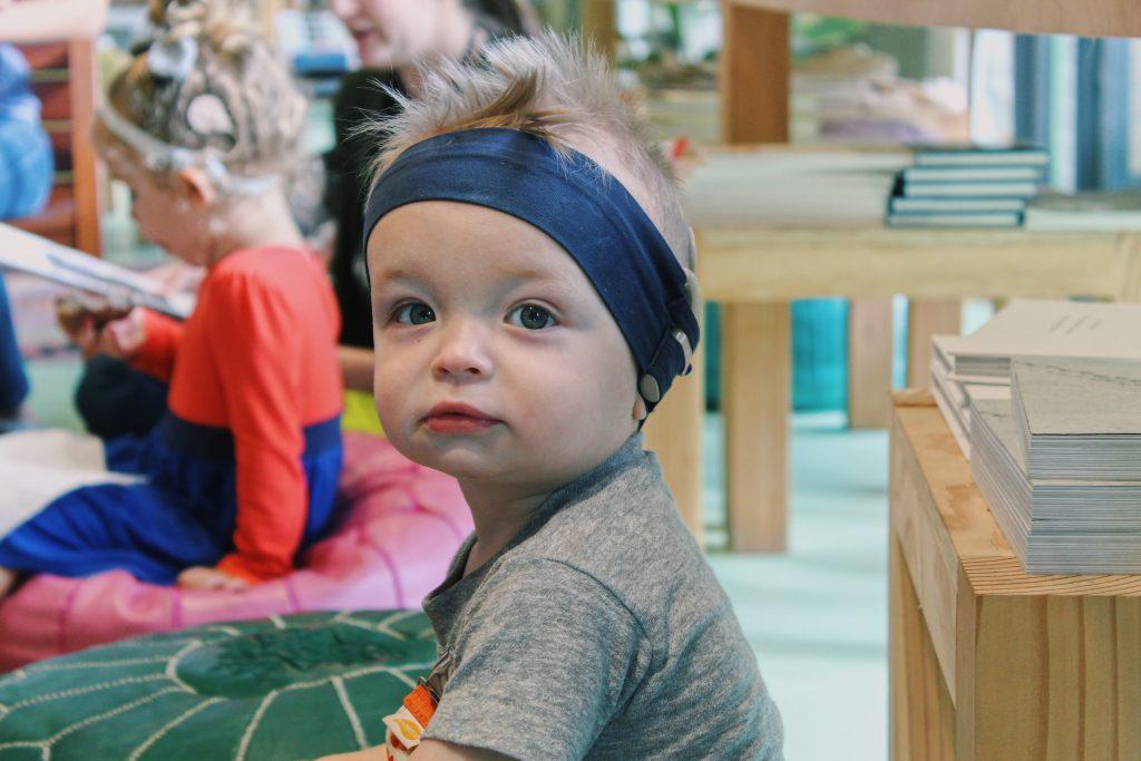 young boy smiling and playing on ground, wearing a headband holding his cochlear implant technology
