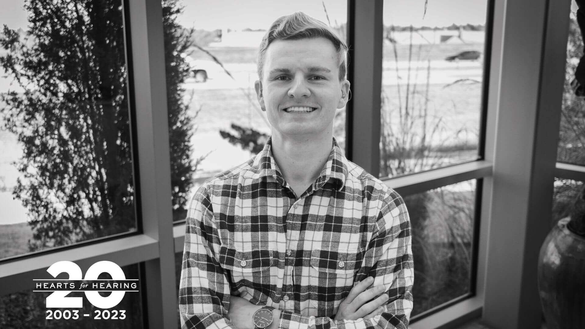 A black and white photo of Peter Hardt smiling with his arms crossed. He is wearing a plaid shirt.