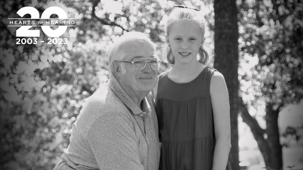 a man kneeling next to a young girl in a dress. They both have hearing aids.