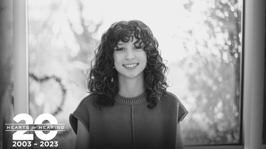 a black and white photo of a girl with dark curly hair infront of a window