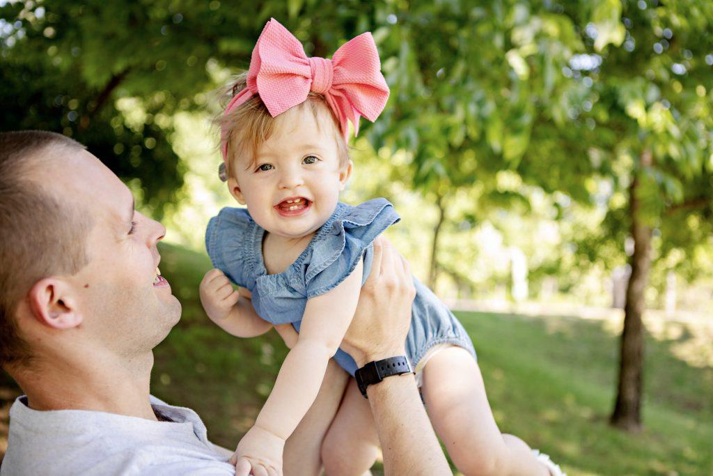 young smiling girl lifted by father's arms smiling with large bow in hair