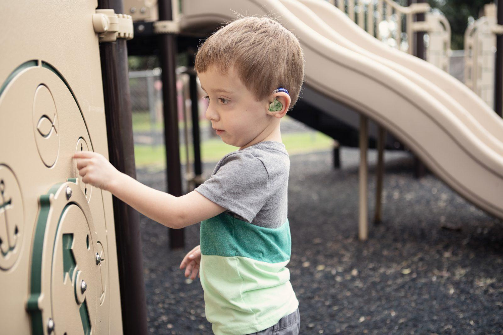 young boy zane wearing hearing aid technology and playing at playground