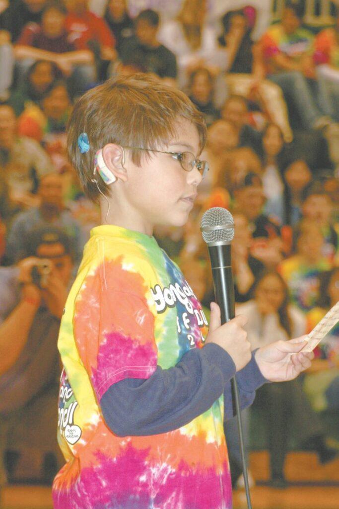 young boy addressing crowd holding a microphone