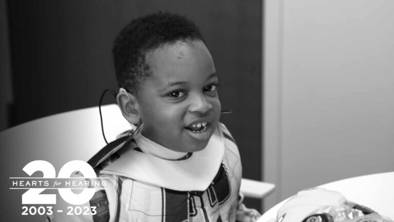 A young boy in a transformer costume with a hearing aid smiles at the camera.