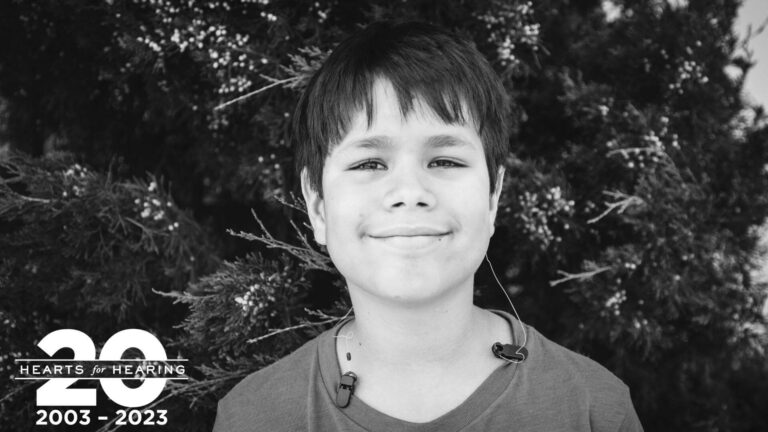 photo of a boy in front of a tree with cochlear implants and an off the ear processor