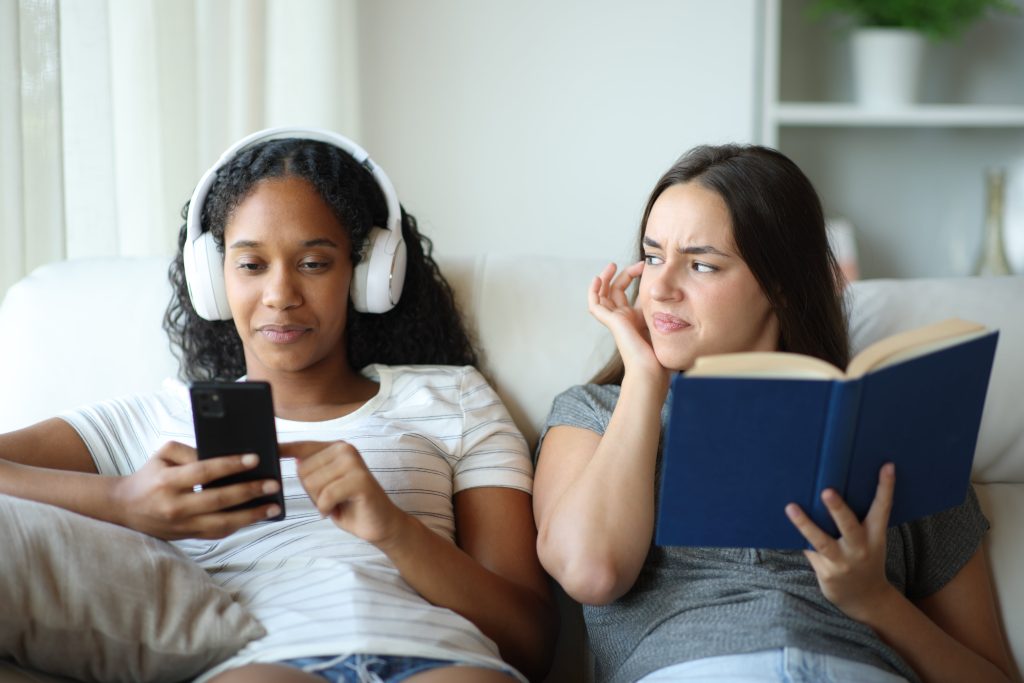 Two females one reading a book and one listening to music.