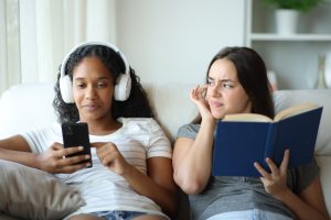 Two females one reading a book and one listening to music.